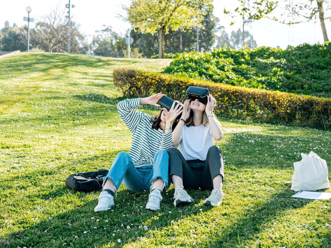 To piger sidder i en park med VR briller på