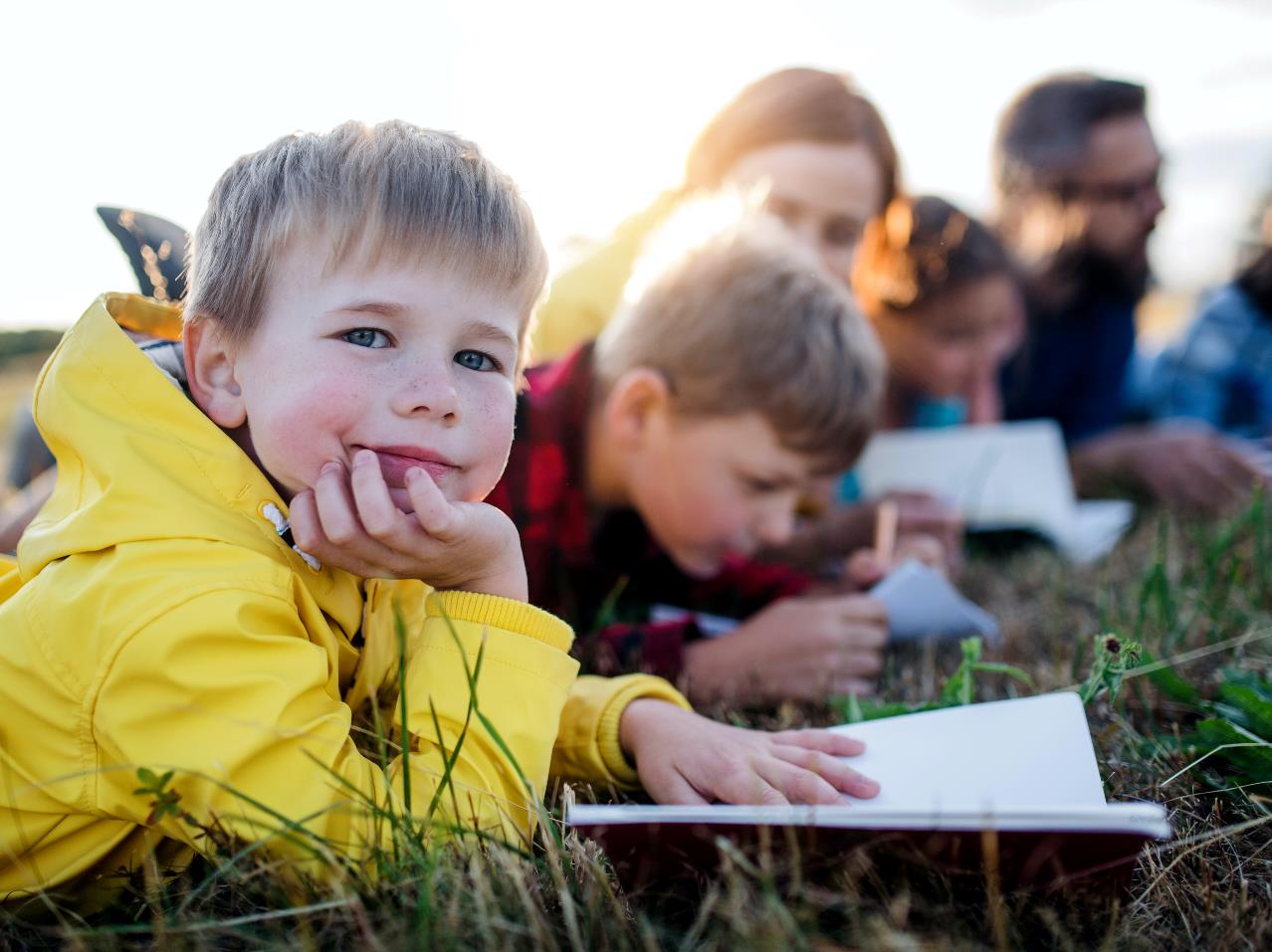 Lille dreng ligger i græsset med en bog sammen med andre elever